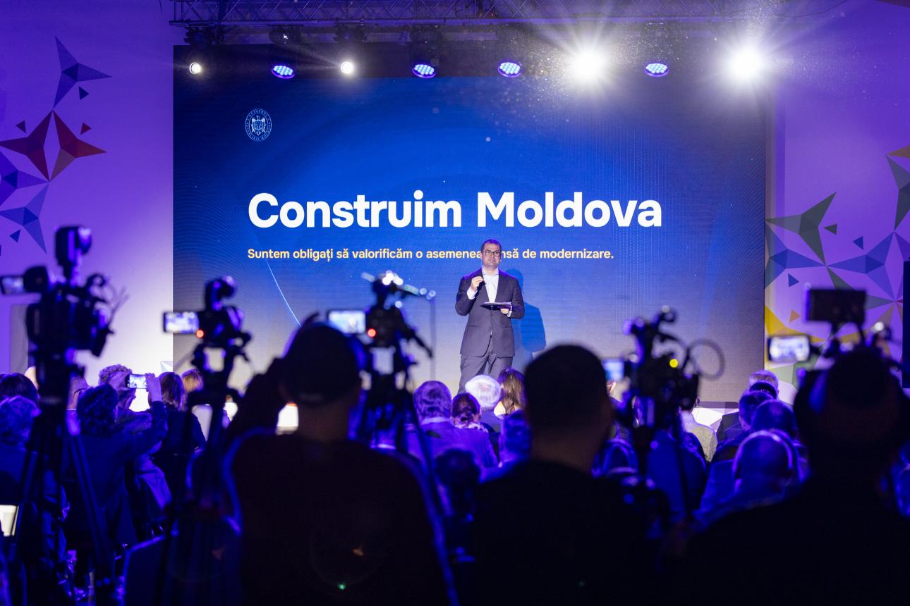 Un vorbitor cu microfon pe scena evenimentului Construim Moldova, în fața publicului și a camerelor de filmat