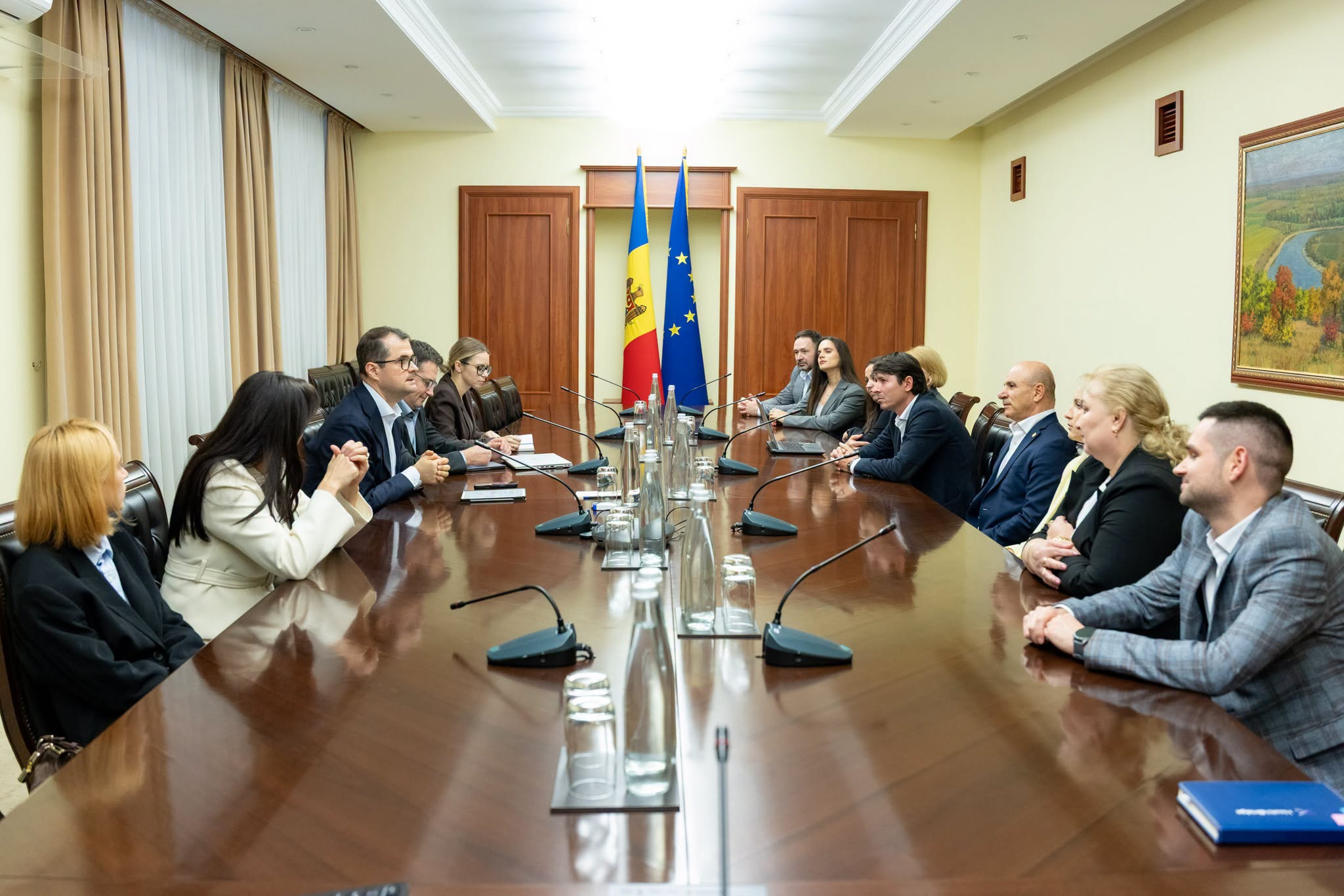 Participanți așezați la o masă de ședință cu microfoane, în fața drapelelor Republicii Moldova și Uniunii Europene
